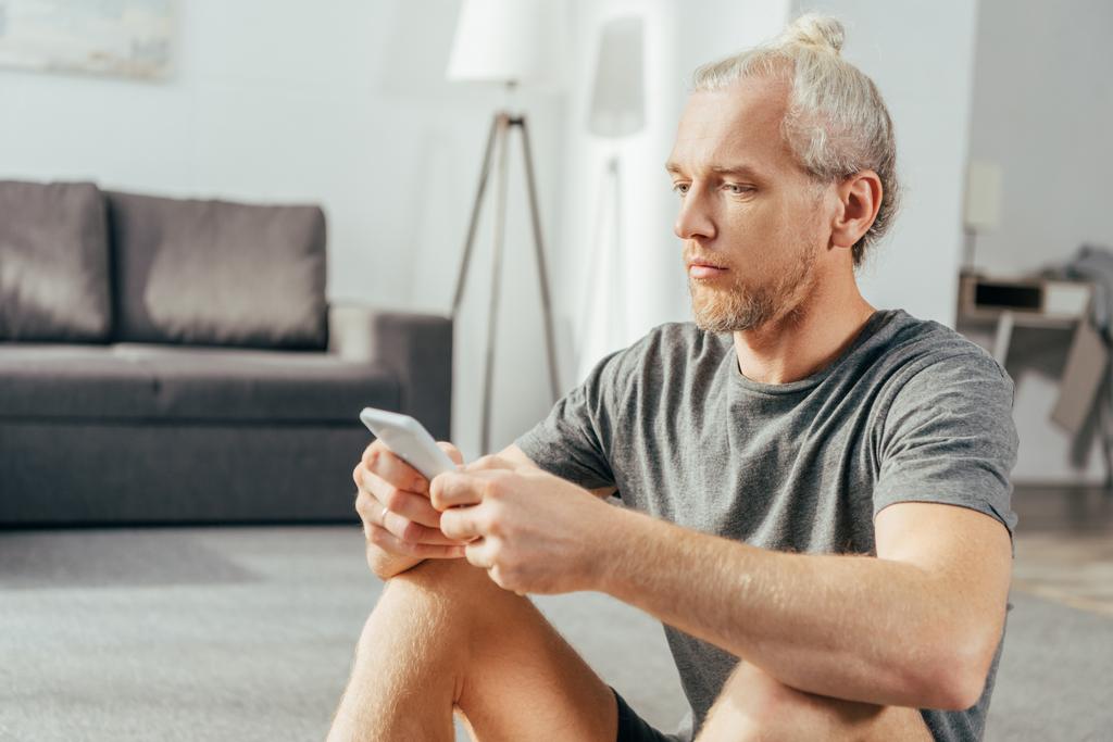 vakava aikuinen mies urheiluvaatteissa istuu ja käyttää älypuhelinta kotona
 - Valokuva, kuva