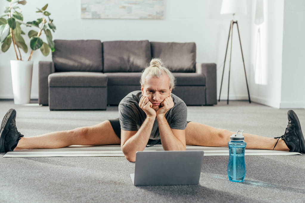 sporty adult man doing split exercise and looking at laptop - Photo, Image