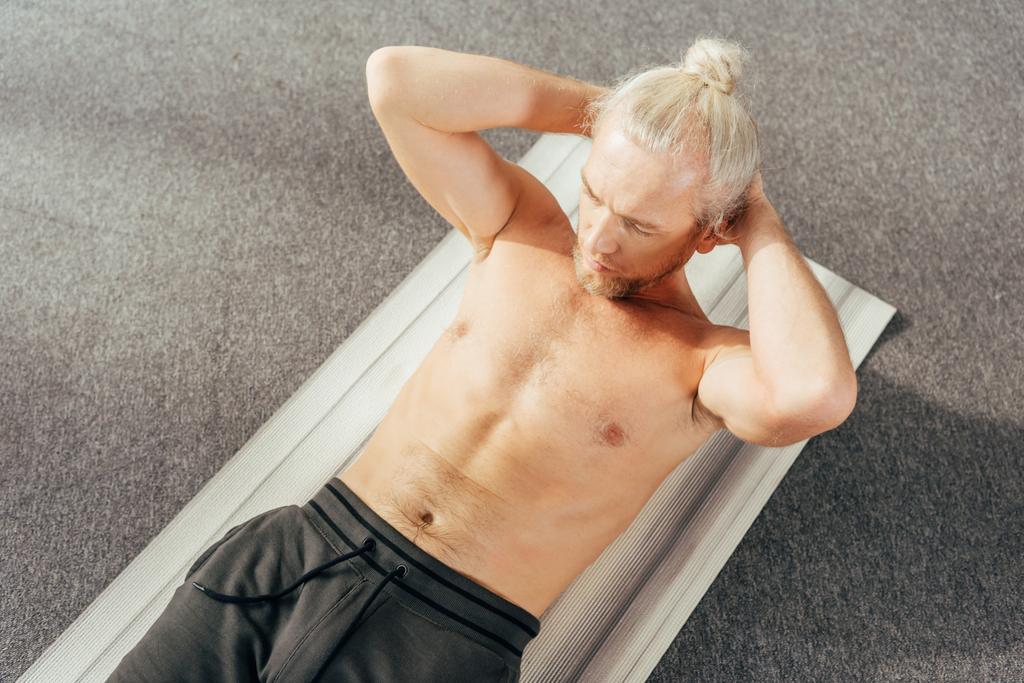 высокий угол зрения человек без рубашки делать упражнения ABS на коврик для йоги у себя дома
 - Фото, изображение