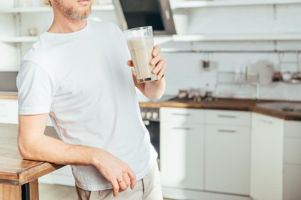 обрезанный снимок спортивного человека, держащего стакан с протеиновым коктейлем дома
 - Фото, изображение