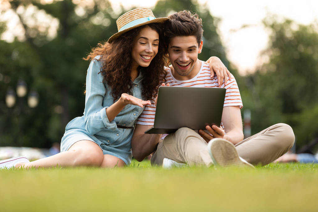 幸せなカップルの男と公園の芝生の上に座ってラップトップを使用して女性のイメージ - 写真・画像