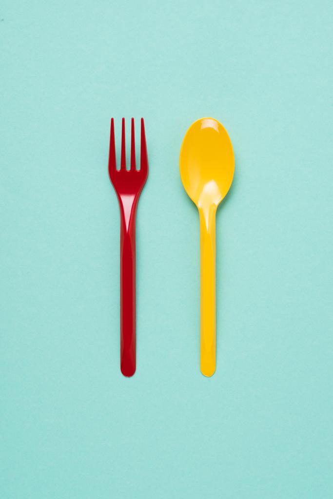 Bovenaanzicht van rode plastic vork en gele lepel op blauwe achtergrond - Foto, afbeelding