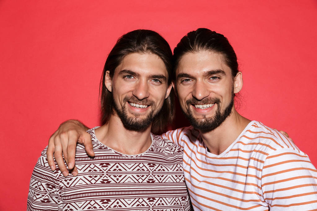 Portret dwóch braci twin szczęśliwy młody na białym tle nad czerwonym tle, przytulanie - Zdjęcie, obraz