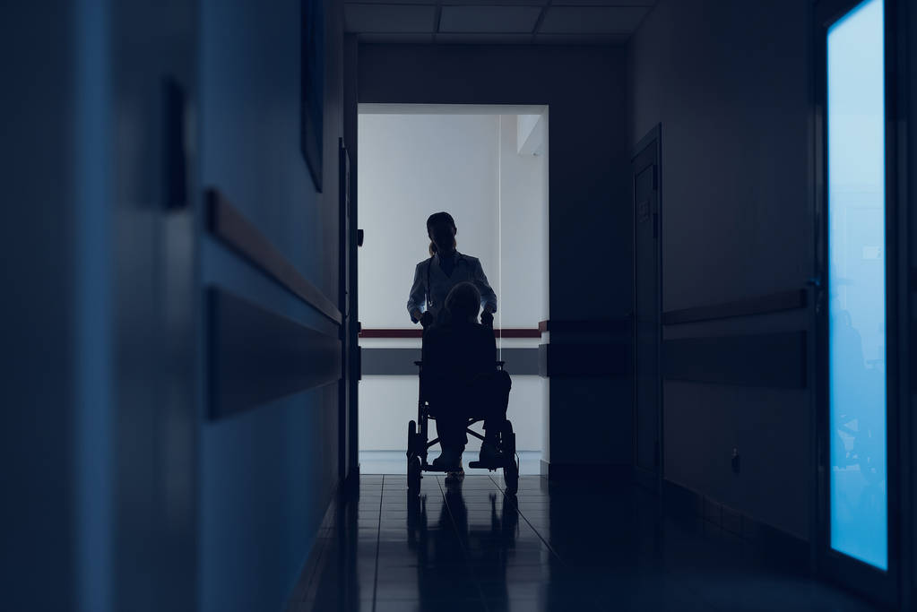 Sairaanhoitaja työntää pyörätuolia potilaan kanssa sairaalassa
 - Valokuva, kuva