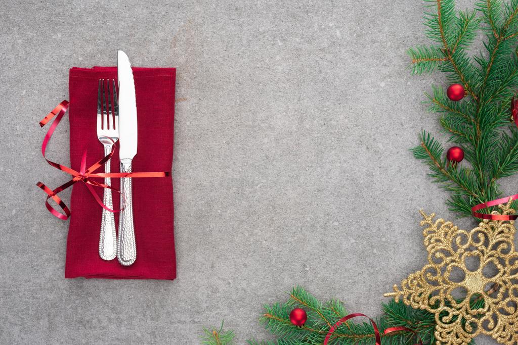 vista elevada de tenedor y cuchillo envuelto por cinta roja en la mesa con rama de hoja perenne decorada con bolas de Navidad y estrella de Navidad dorada
 - Foto, imagen