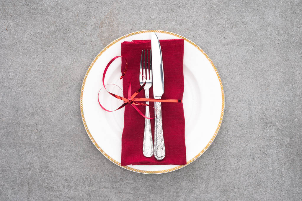 vlakke leggen met geserveerd plaat met vork en mes verpakt door rode feestelijk lint op grijze oppervlak - Foto, afbeelding