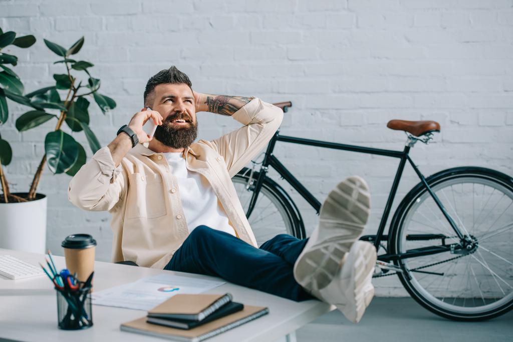 Erfolgreicher Geschäftsmann spricht auf Smartphone mit Beinen auf dem Schreibtisch - Foto, Bild