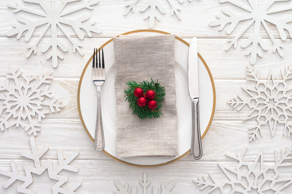 верхний вид тарелки с вилкой, ножом и вечнозеленой веткой с рождественскими шарами в окружении украшенных снежинками
  - Фото, изображение