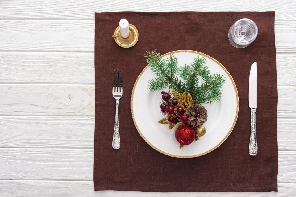 ワイン グラス、皿、フォーク、ナイフ、スプーン、テーブル クロスにキャンドルとクリスマスの装飾を持つ提供テーブルのトップ ビュー  - 写真・画像