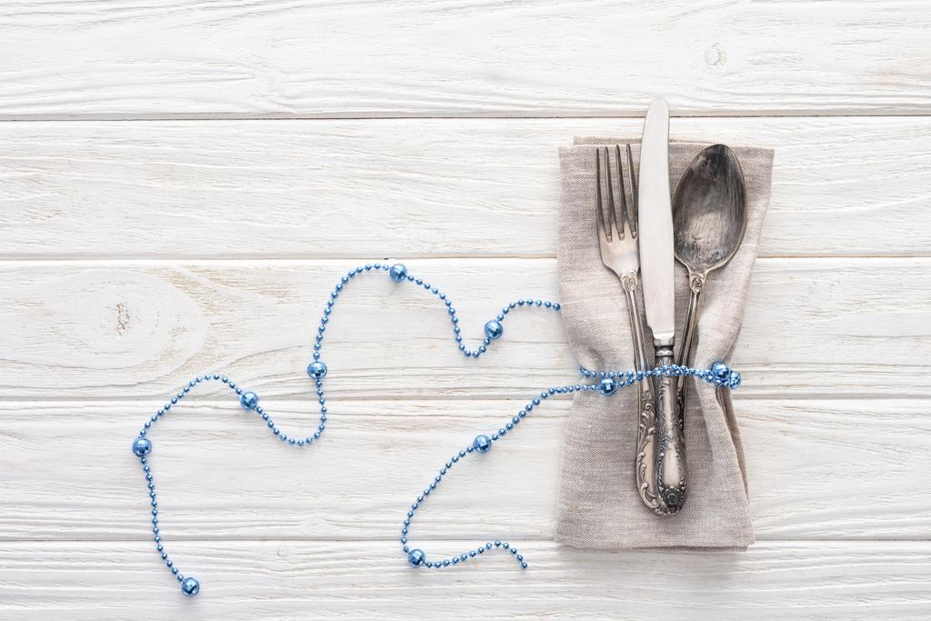 Nézd meg felülről a villát, kést és kanalat csomagolva a fából készült asztal dekoratív kék gyöngy - Fotó, kép