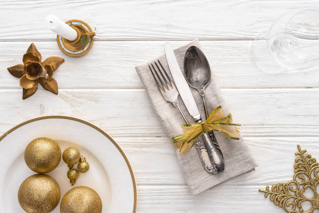 vista dall'alto del piatto con palline di Natale dorate, candela e forchetta, cucchiaio, coltello avvolto dal nastro sul tavolo di legno
  - Foto, immagini