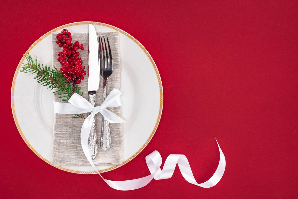 vista dall'alto di piatto con ramo di pino, bacche, forchetta e coltello avvolto da nastro su piatto isolato su rosso
 - Foto, immagini
