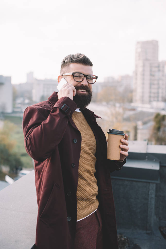 stylowe dojrzałego mężczyzny w okularach rozmowy na smartfonie i przytrzymując kawy na dachu - Zdjęcie, obraz