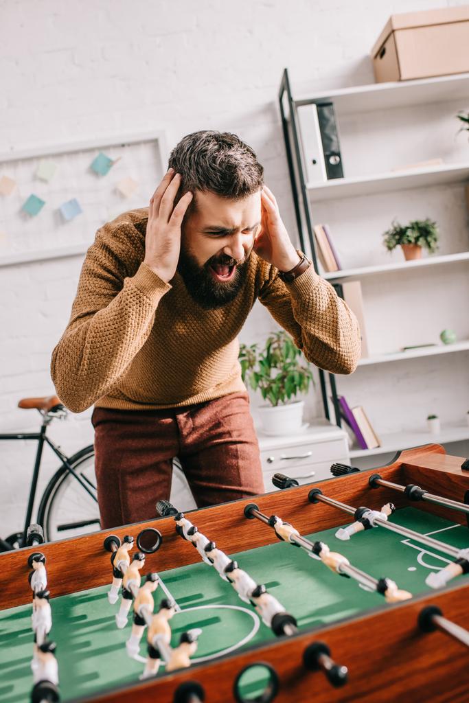 irritado adulto homem com as mãos na cabeça gritando e jogando jogo de futebol de mesa em casa
 - Foto, Imagem