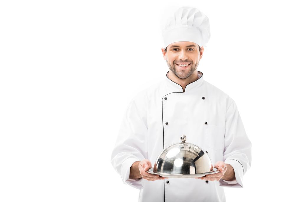 sonriente joven chef sosteniendo bandeja de servir con cúpula y mirando a la cámara aislada en blanco
 - Foto, imagen
