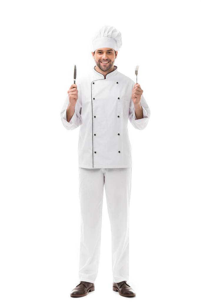 usmívající se mladý kuchař hospodářství nůž a vidličku a při pohledu na fotoaparát izolované na bílém - Fotografie, Obrázek