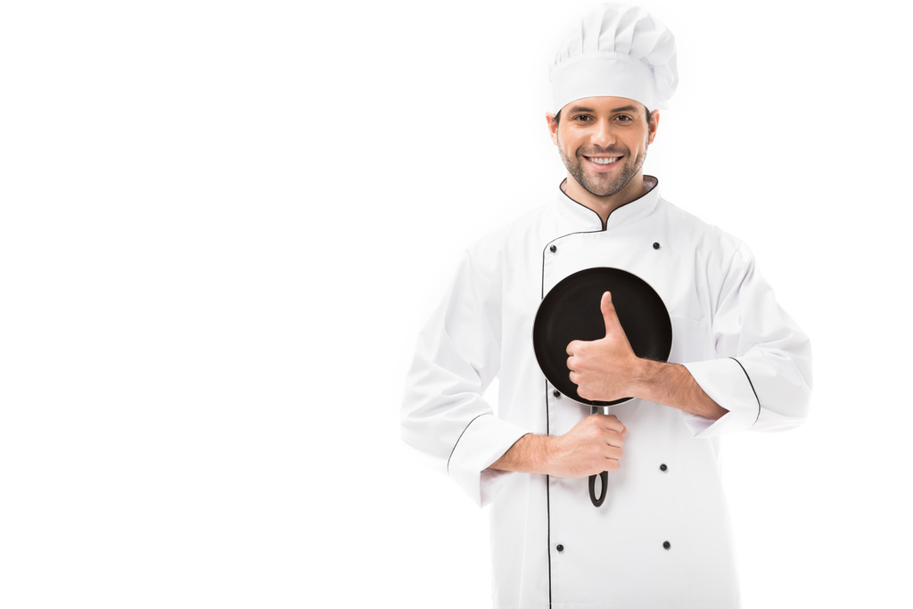 χαμογελαστός νεαρός σεφ κρατώντας το τηγάνι και να δείχνει τον αντίχειρα επάνω απομονωθεί σε λευκό - Φωτογραφία, εικόνα