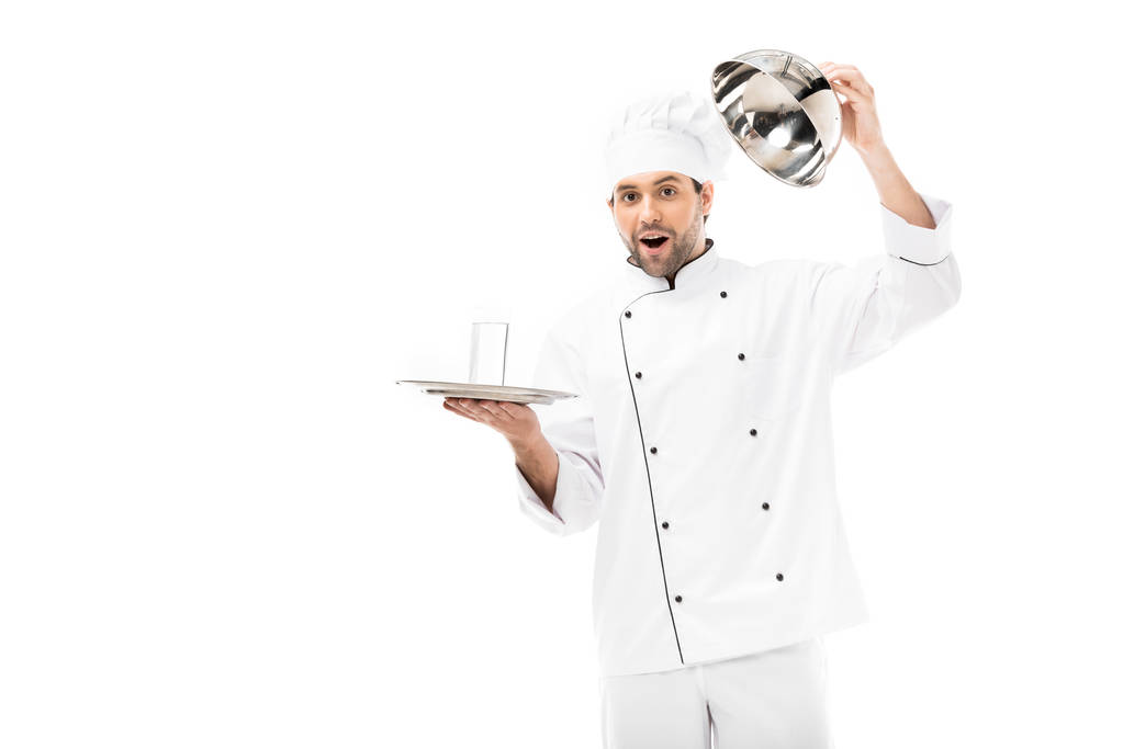 verrast jonge chef-kok openen seving koepel met glas water binnen geïsoleerd op wit - Foto, afbeelding