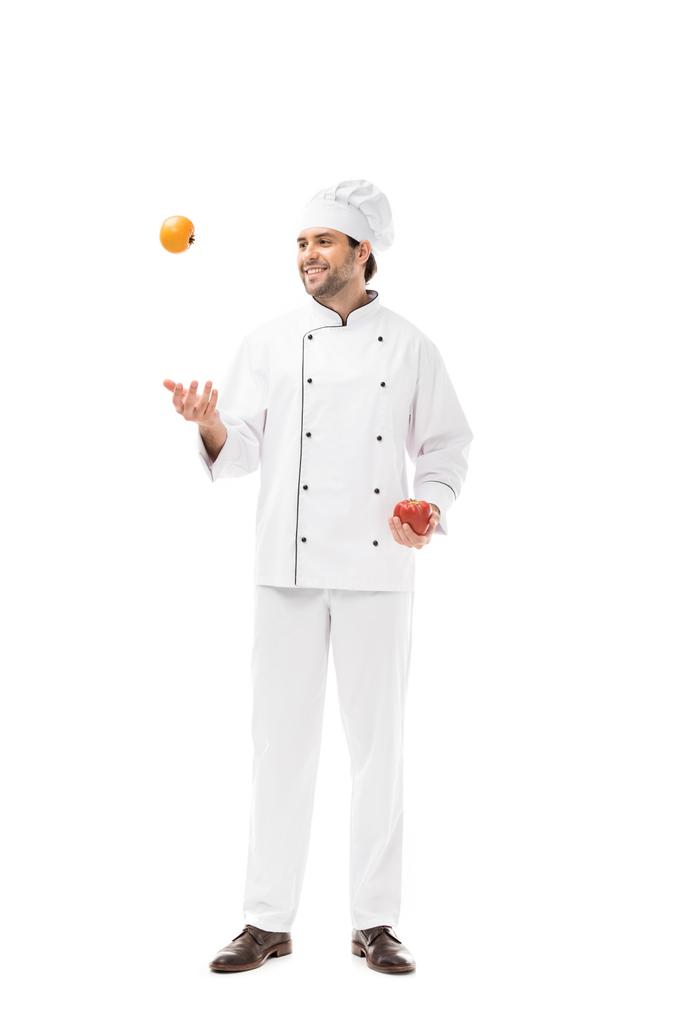 happy young chef juggling with tomato and bell pepper isolated on white - Photo, Image