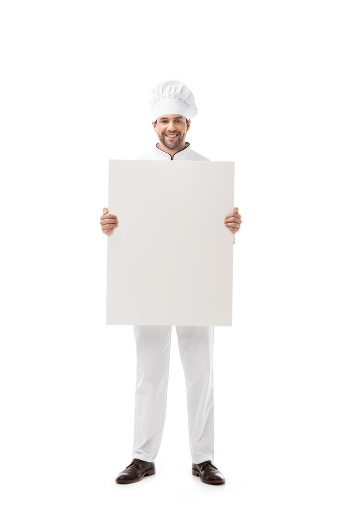 pohledný mladý kuchař drží prázdný nápis a usmívá se na kameru izolované na bílém  - Fotografie, Obrázek