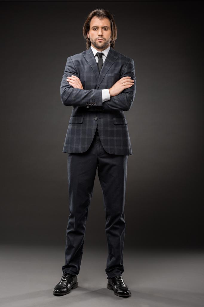 уверенный бизнесмен, стоящий со скрещенными руками и смотрящий в камеру на черном
 - Фото, изображение