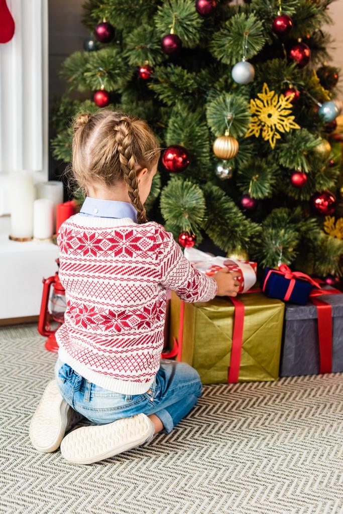 Achteraanzicht van schattige jongen openen geschenkdozen onder kerstboom - Foto, afbeelding