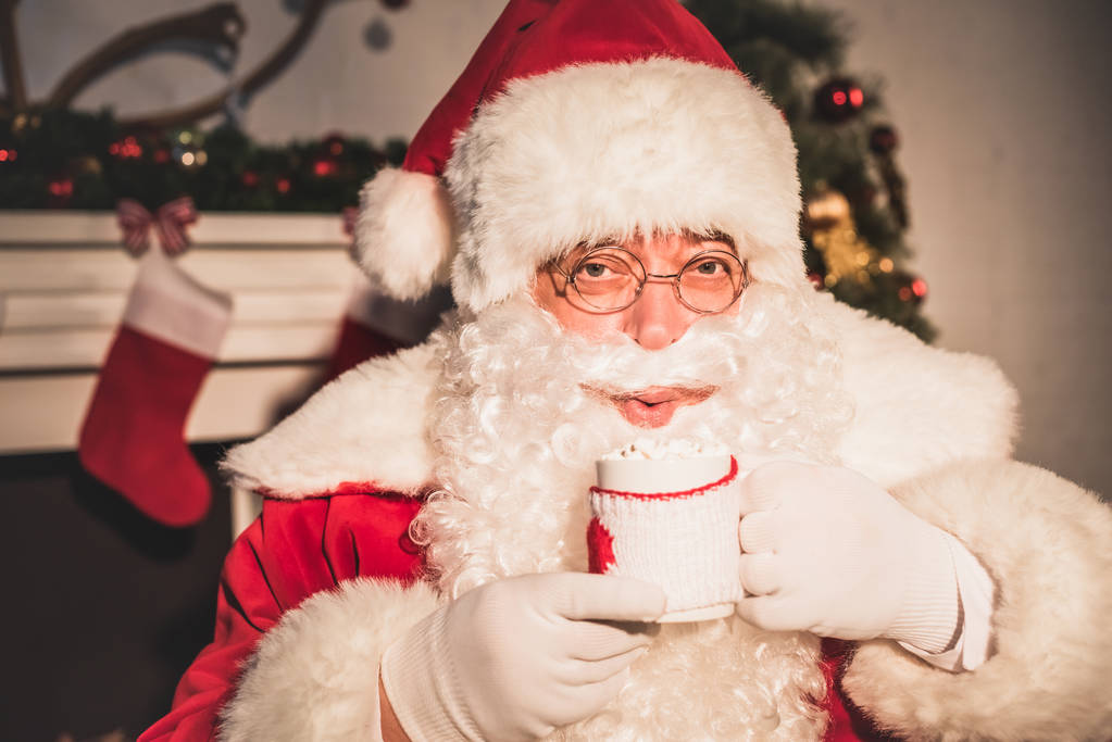 Santa drinken warme drank met marshmallows en camera te kijken - Foto, afbeelding