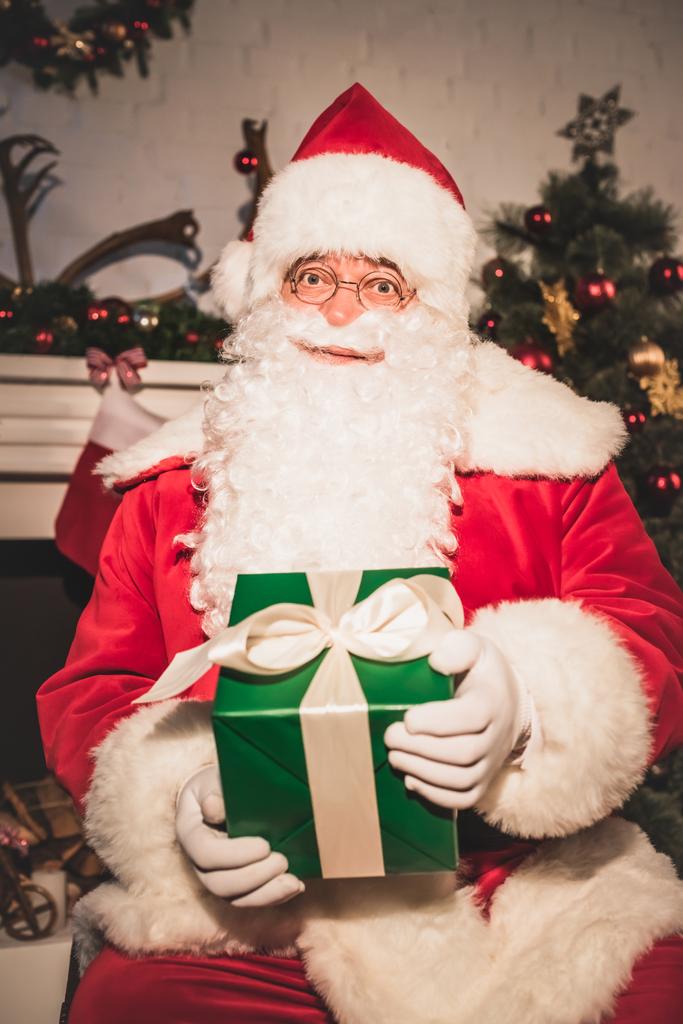 Santa claus trzyma prezent na Boże Narodzenie i patrząc na kamery  - Zdjęcie, obraz