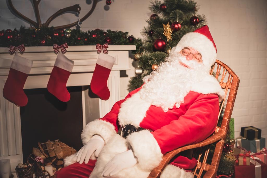Άγιος Βασίλης κοιμάται στο ρηλάξ κοντά στο τζάκι με κάλτσες - Φωτογραφία, εικόνα
