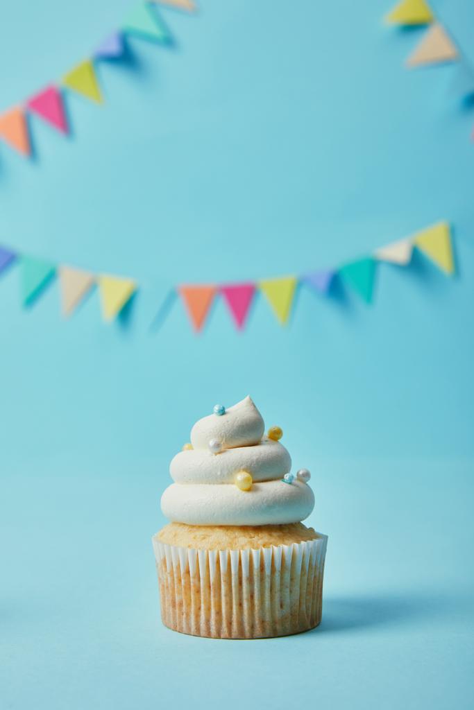 Delicioso cupcake com açúcar polvilha no fundo azul com bunting
 - Foto, Imagem