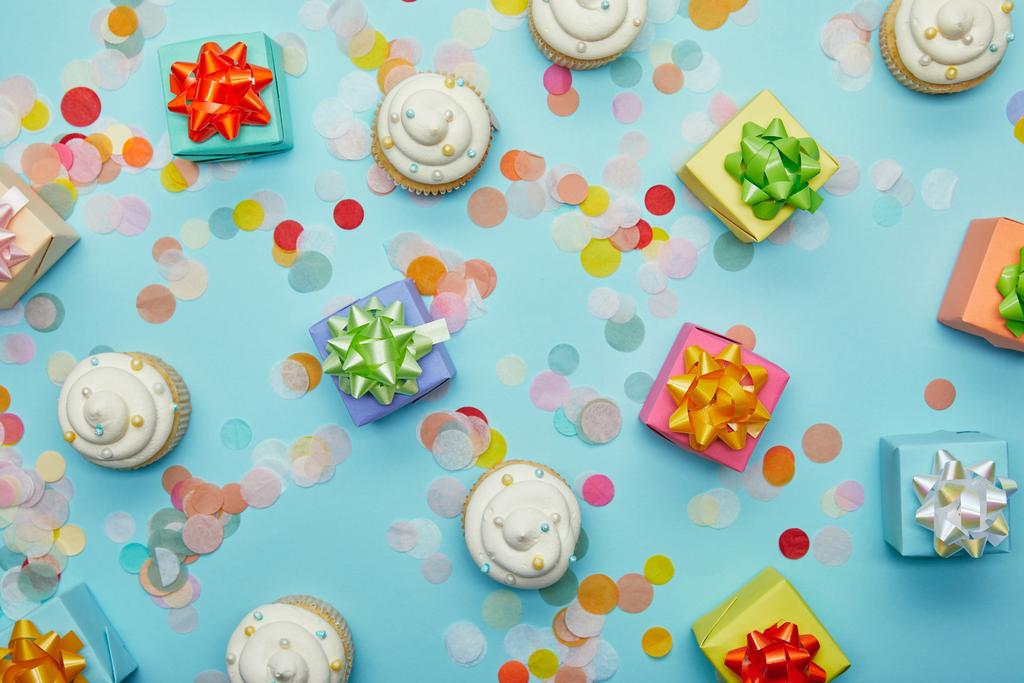 Top view of delicious cupcakes, confetti and gifts on blue background - Photo, Image