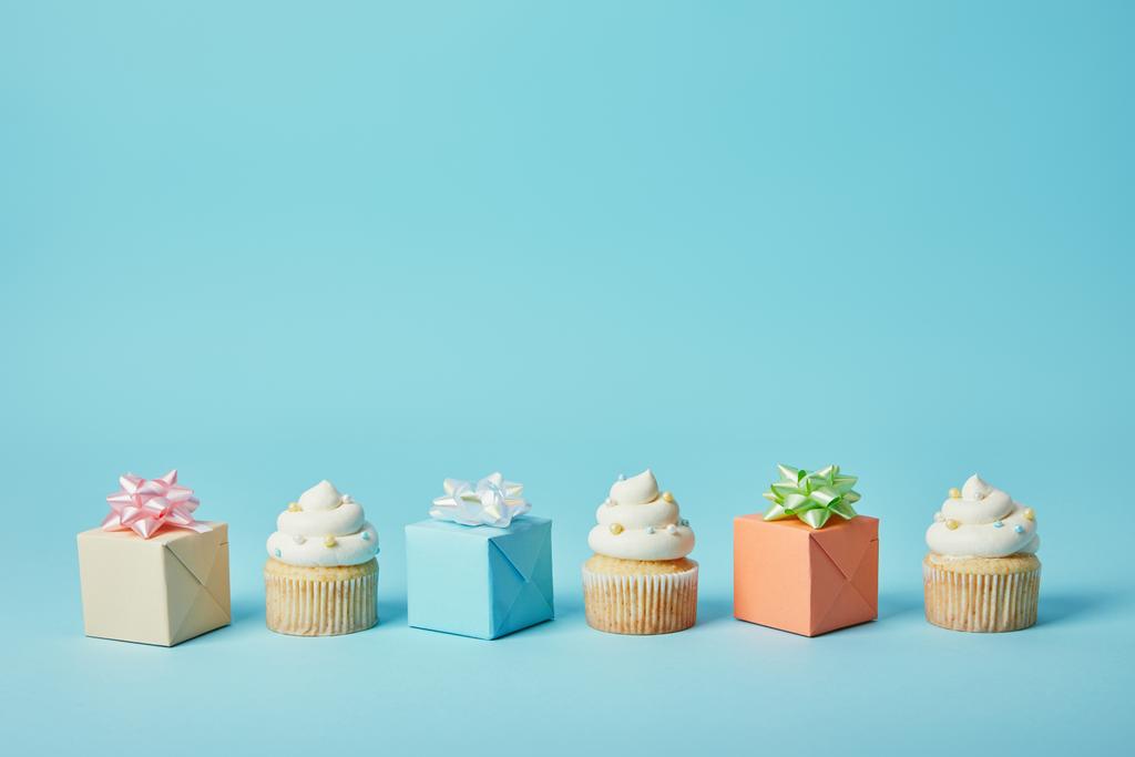 Delicious cupcakes and diffrent gifts on blue background - Photo, Image