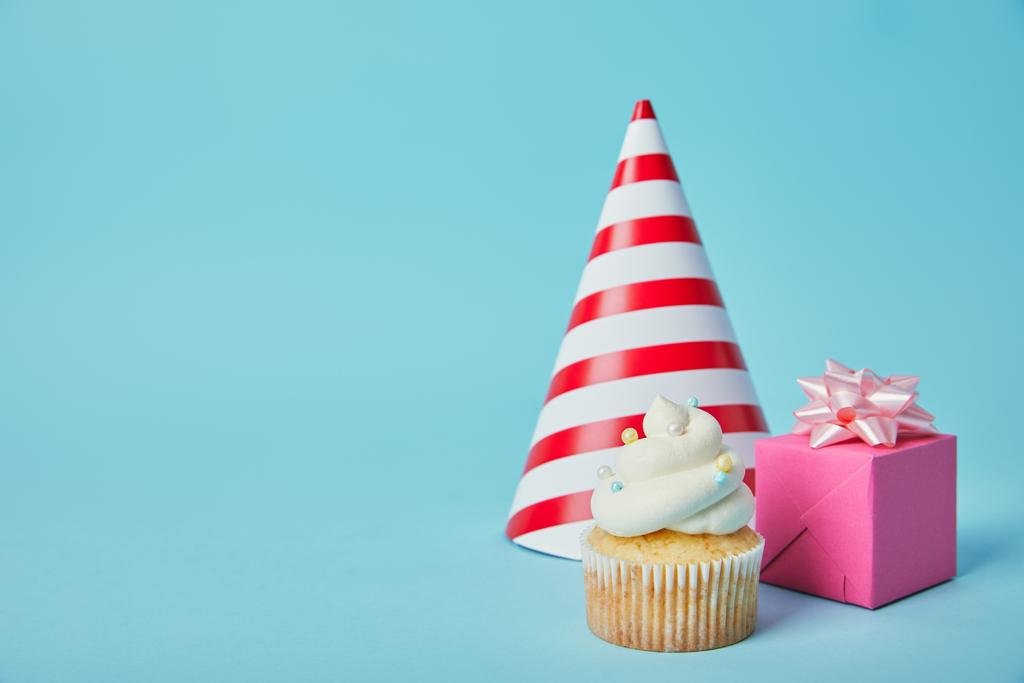 Kırmızı beyaz parti şapkası, pembe hediye kutusu ve mavi zemin üzerine lezzetli kek - Fotoğraf, Görsel