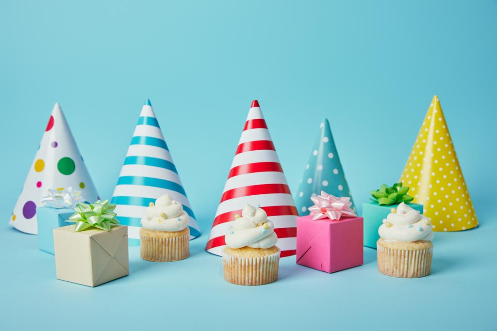 Colorful party hats, gifts and delicious cupcakes on blue background - Photo, Image