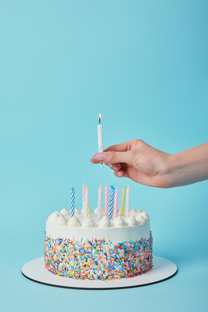 Vista parziale della donna che mette la candela di illuminazione sulla torta di compleanno su sfondo blu
 - Foto, immagini