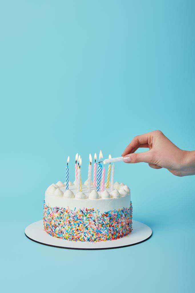 Vista parcial de la mujer encendiendo velas en pastel de cumpleaños sobre fondo azul
 - Foto, Imagen