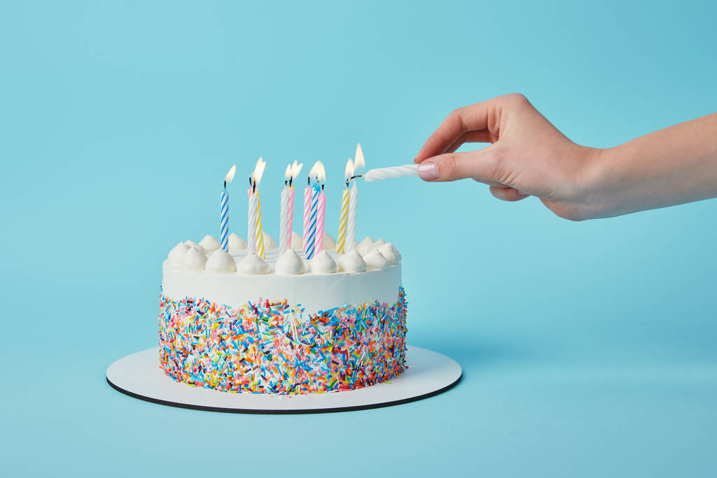 Vista parcial da mulher acendendo velas no bolo de aniversário no fundo azul
 - Foto, Imagem