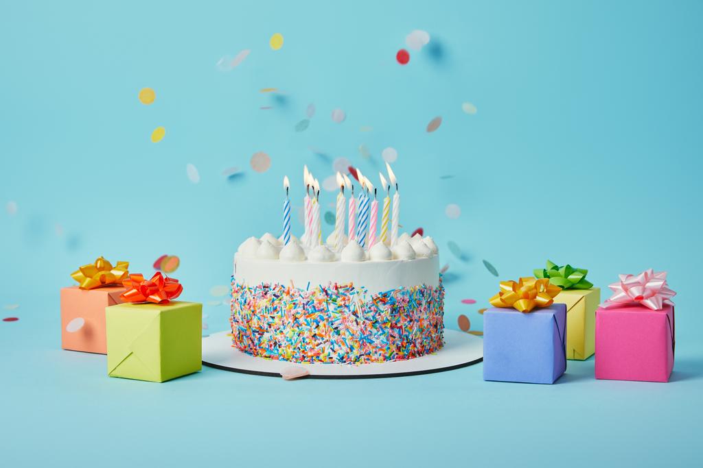 leckere Torte mit Kerzen, bunten Geschenken und Konfetti auf blauem Hintergrund - Foto, Bild