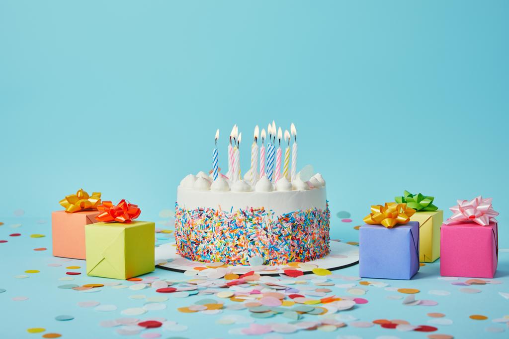 Delicious cake with candles, colorful gifts and confetti on blue background - Photo, Image