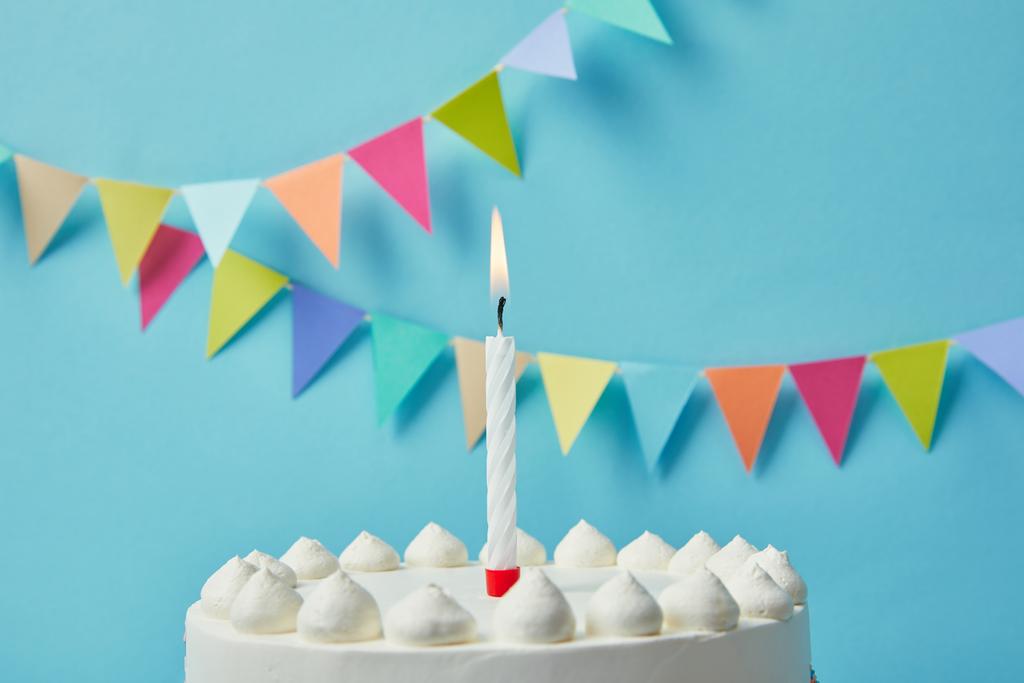 Candle on delicious birthday cake on blue background with bunting - Photo, Image