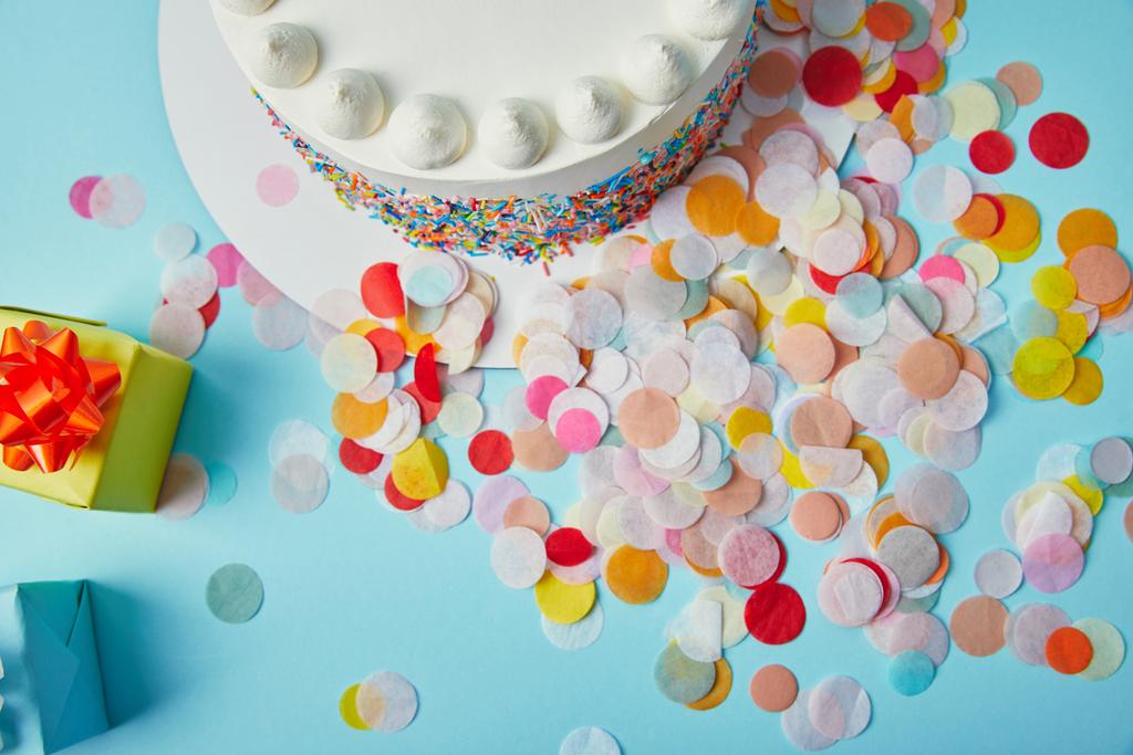 Draufsicht auf köstlichen Kuchen, Geschenke und Konfetti auf blauem Hintergrund - Foto, Bild