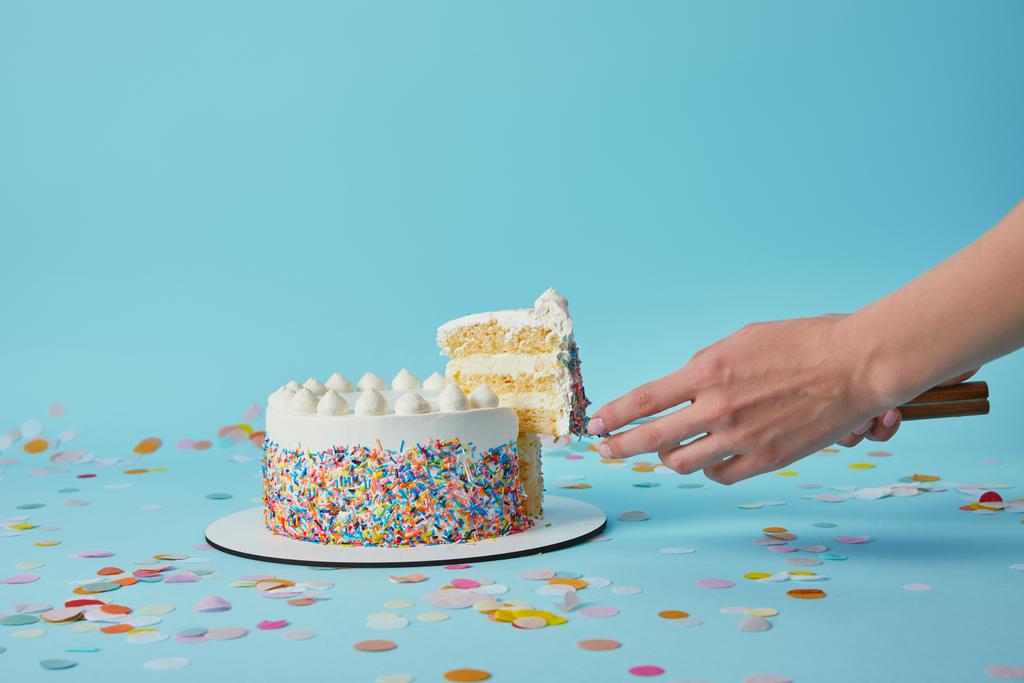 Vista parcial da mulher tomando pedaço de bolo delicioso no fundo azul
 - Foto, Imagem