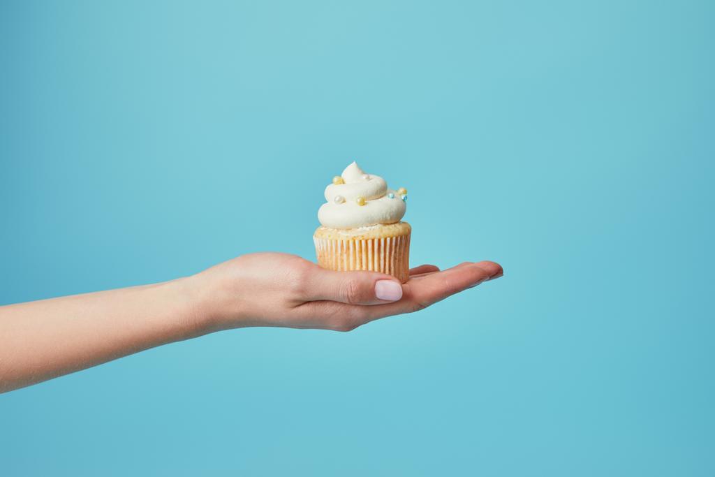 Teilansicht der Frau mit leckerem Cupcake mit Zuckerstreusel auf blauem Hintergrund - Foto, Bild