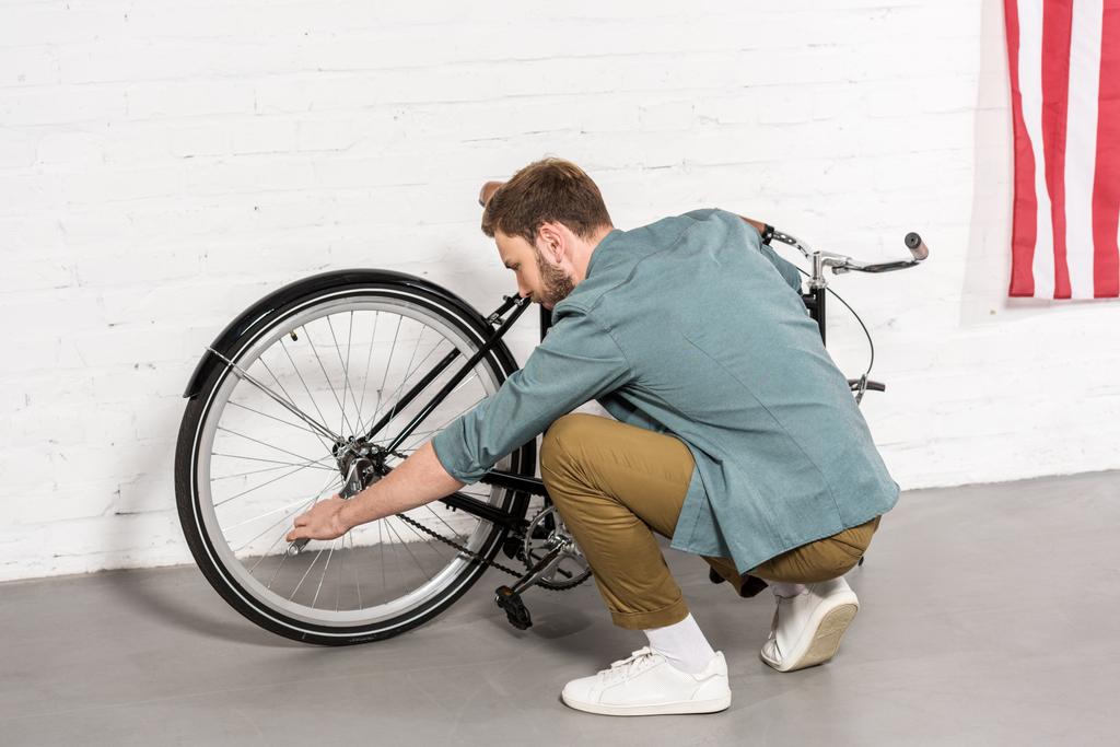 vista lateral del joven reparando la bicicleta con llave ajustable
  - Foto, Imagen
