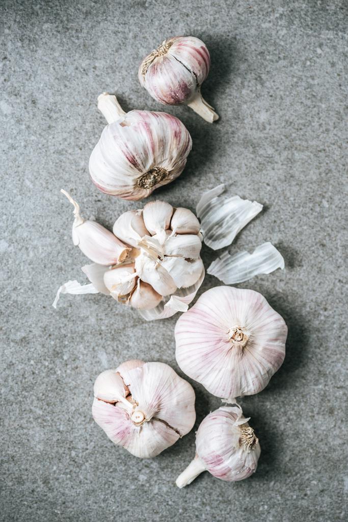 Верхний вид спелых луковиц чеснока и шелухи на сером фоне
 - Фото, изображение