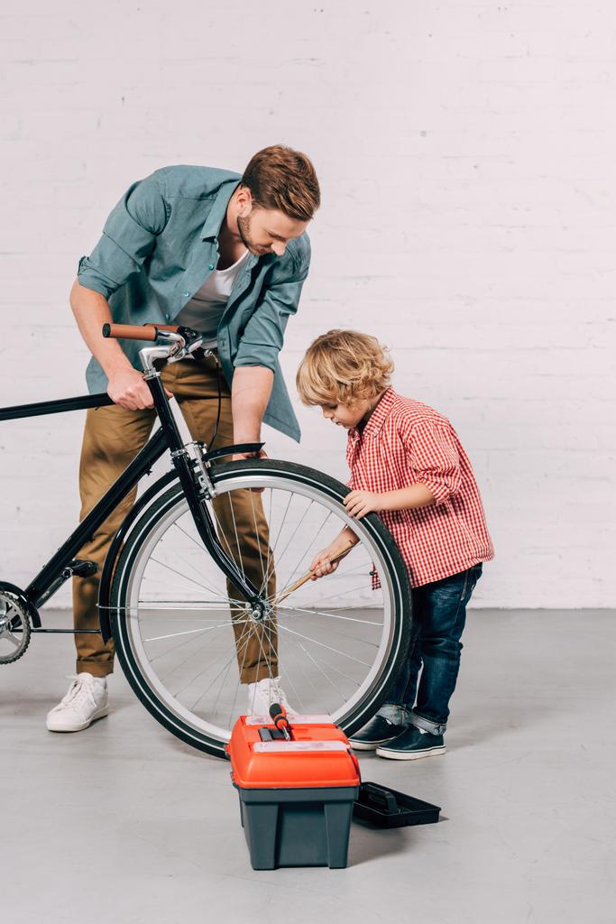 Selektywny fokus chłopca i jego ojca, naprawa koła roweru w warsztacie - Zdjęcie, obraz
