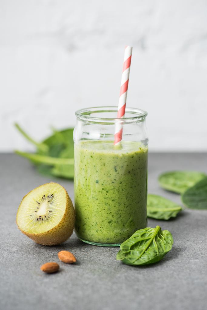 Kiwi, spinazie bladeren en groene biologische smoothie in glas met rietje  - Foto, afbeelding