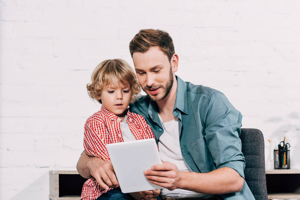 feliz hombre mostrando tableta digital a pequeño hijo en casa
 - Foto, imagen
