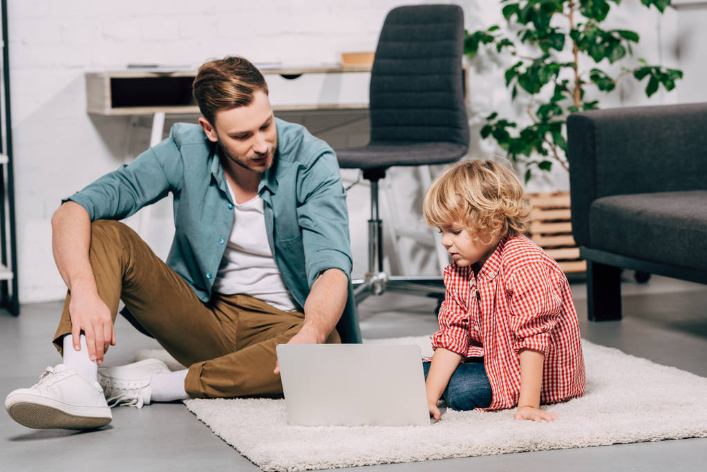 father and son sitting on floor with laptop at home - Photo, Image