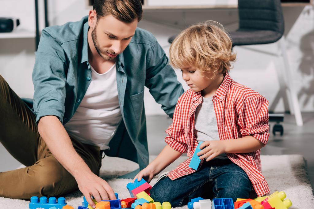 Selektywny fokus dziecko i jego ojciec, grając z kolorowe bloki z tworzyw sztucznych na piętrze w domu - Zdjęcie, obraz